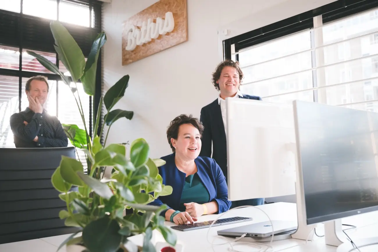 Drie Brthrs-collega's kijken samen lachend naar een scherm